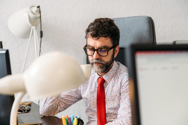 Geschäftsmann mittleren Alters mit Bart und Brille beim Kaffeetrinken im Büro