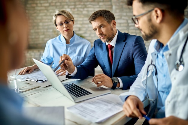 Geschäftsmann mittleren Alters und Gruppe von Ärzten, die während eines Meetings an einem Computer arbeiten