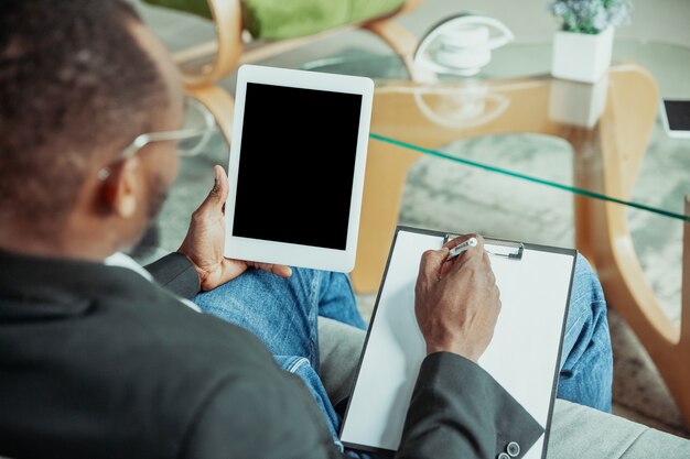 Geschäftsmann oder Student, der von zu Hause aus arbeitet, wird isoliert oder hält Quarantäne wegen des Coronavirus. Afroamerikanischer Mann mit Laptop, Tablet und Kopfhörern. Online-Konferenz, Unterricht, Remote-Office.