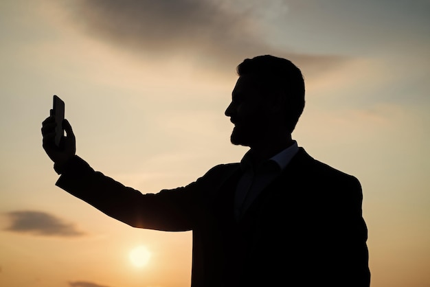 Geschäftsmann Silhouette macht Selfie am Telefon auf Himmelshintergrund Vertrauen und Erfolg erfolgreiche Zukunft agiles Geschäft Einsamkeit braucht die Inspiration Mann fühlt Motivation moderne Technologie