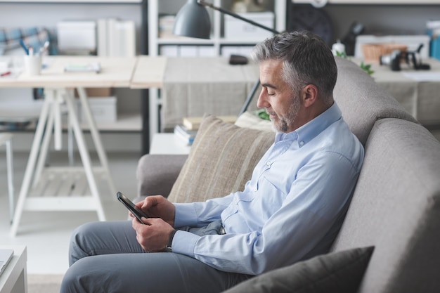 Geschäftsmann sitzt auf der Couch und schreibt SMS mit seinem Touchscreen-Smartphone