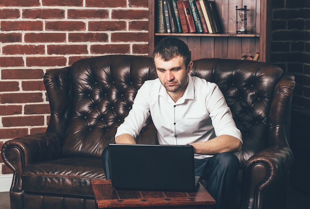 Geschäftsmann sitzt auf einem Ledersofa hinter einem Laptop auf Rauminnenraum. Ein Mann arbeitet in einem eigenen Schrank