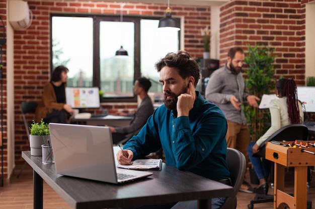 Geschäftsmann spricht mit Leiter über Kopfhörer und schreibt Marketingstrategie in die Zwischenablage, während er geschäftliche Zusammenarbeit im Startup-Büro plant. Unternehmer, der am Managementprojekt arbeitet