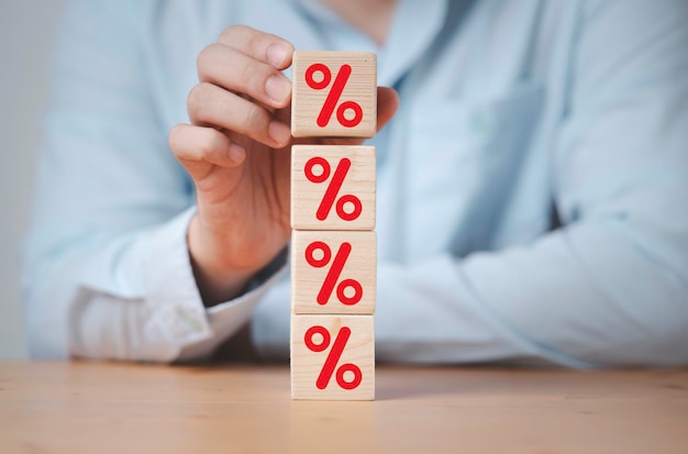 Geschäftsmann stapelt rotes Prozentzeichen auf Holzwürfelblock für die Finanzplanung von Zinssatz- und Hypothekenrankingkonzept