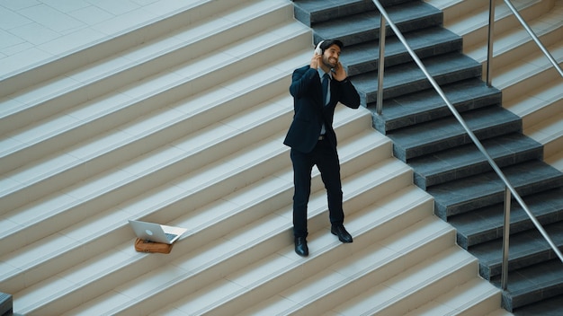 Geschäftsmann steht auf der Treppe und bewegt sich zu Musik von Kopfhörern aus.