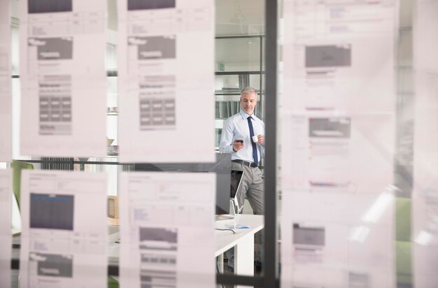 Foto geschäftsmann steht im büro, trinkt büro, benutzt smartphone