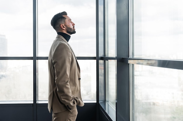 Geschäftsmann steht und schaut aus dem Fenster im Profilfoto des Büros