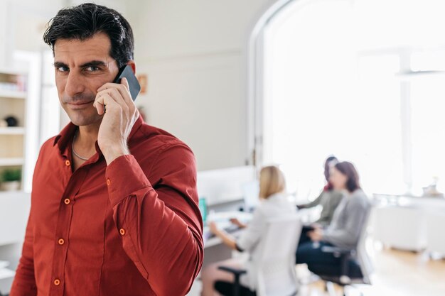 Geschäftsmann telefoniert im Büro mit Kollegen, die im Hintergrund arbeiten