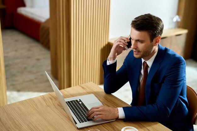 Geschäftsmann telefoniert, während er im Hotelzimmer am Laptop arbeitet