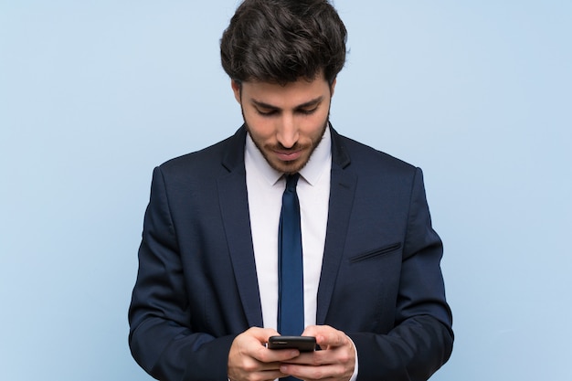 Geschäftsmann über der lokalisierten blauen Wand, die eine Mitteilung mit dem Mobile sendet