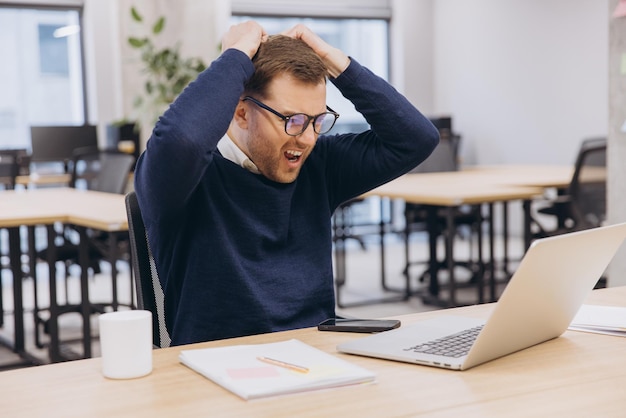 Geschäftsmann wird gestresst und zieht sich an den Haaren, während er mit seinem Laptop im Büro arbeitet, er schreit und schreit