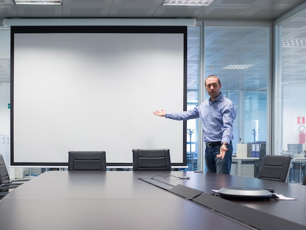 Geschäftsmann zeigt auf den Projektionsbildschirm, während er im Vorstandsaal im Büro steht