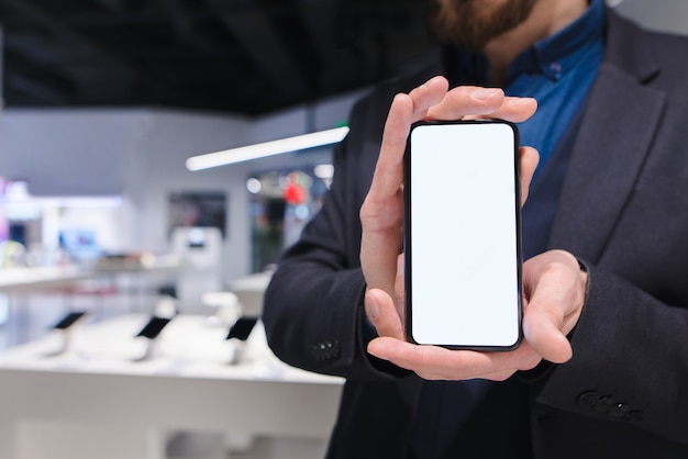 Foto geschäftsmann zeigt ein trendiges smartphone vor dem hintergrund eines elektronikgeschäfts.