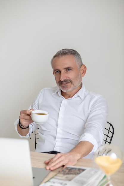 Geschäftsmann. Zuversichtlich gottaussehender Geschäftsmann, der Morgenkaffee im Büro trinkt