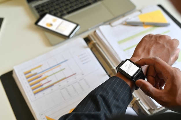 Geschäftsmannanalysedaten in der intelligenten Uhr auf Schreibtisch.