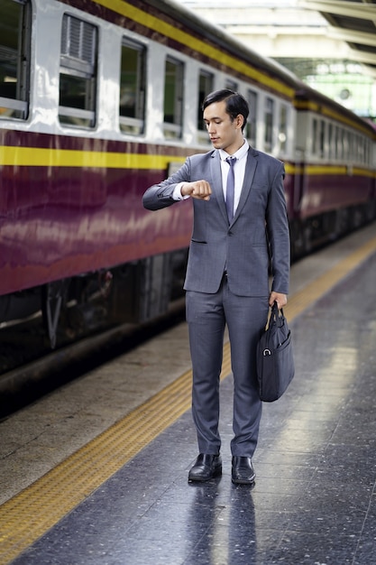 Foto geschäftsmannblick auf armbanduhren und wartende untergrundbahn. schöner mann in anzug und tasche s