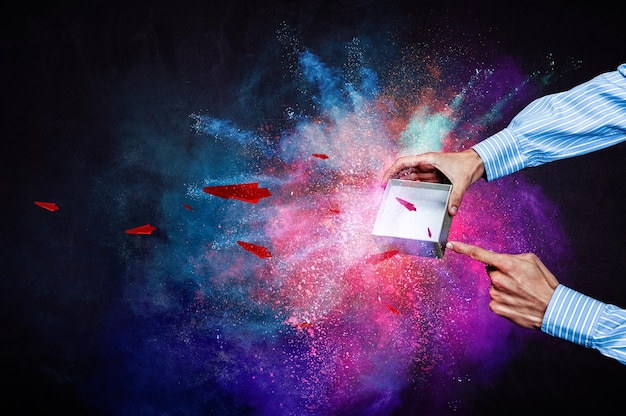 Geschäftsmannhände, die eine kleine magische Papierschachtel mit wegfliegenden Papierflugzeugen halten, gemischte Medien
