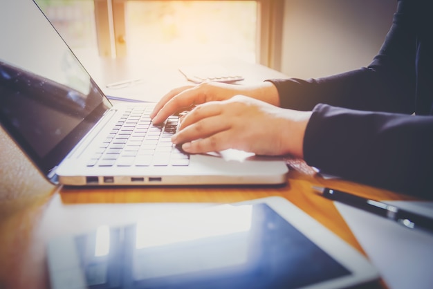 Geschäftsmannhand, die an intelligentem Telefon- und Laptop-Computer arbeitet und Geschäftsdiagramminformationsdiagramm auf Holztisch mit Fensterreflexion im Büro.