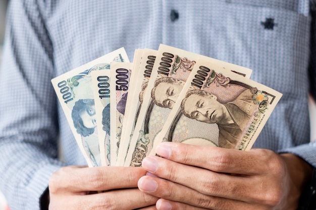 Geschäftsmannhand, die Banknotenstapel der japanischen Yen hält. Geschäfts-, Geld-, Investitions-, Finanz- und Zahlungskonzepte