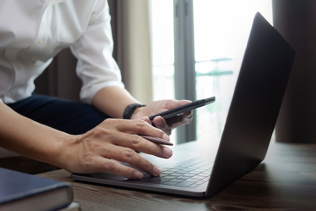 Geschäftsmannhand mit Laptop und Smartphone, die im Home Office arbeiten