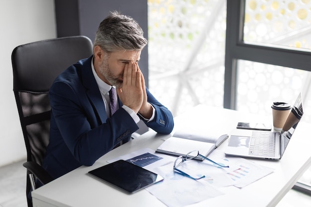 Foto geschäftsmisserfolg deprimierter geschäftsmann mittleren alters, der am schreibtisch im büro sitzt