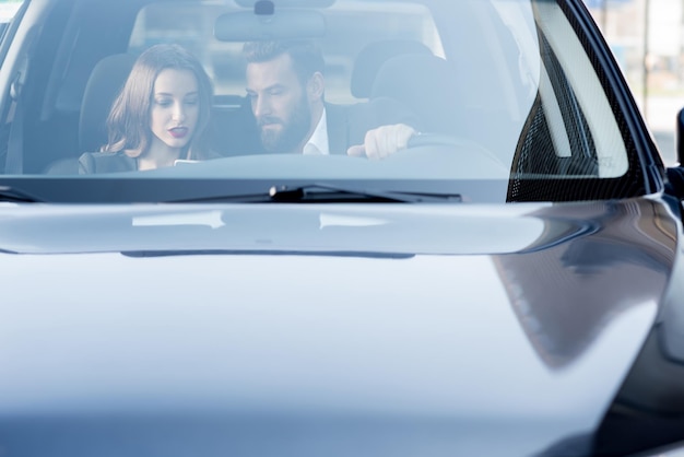 Geschäftspaar, das ein Gespräch beim Autofahren führt. Frontansicht durch die Windschutzscheibe