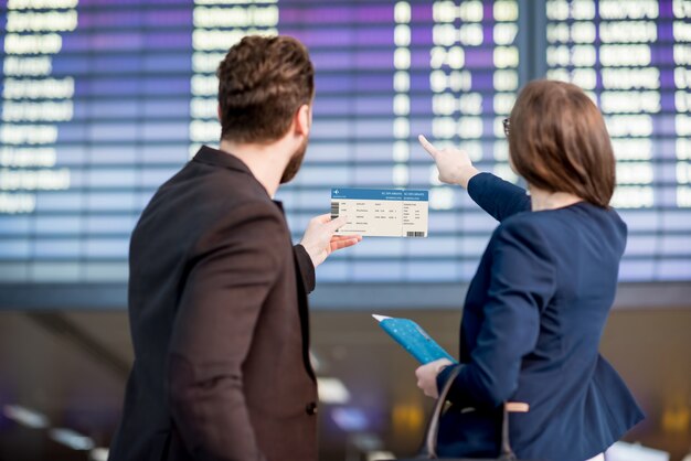 Geschäftspaar mit Blick auf den Fahrplan mit Bordkarte am Flughafen