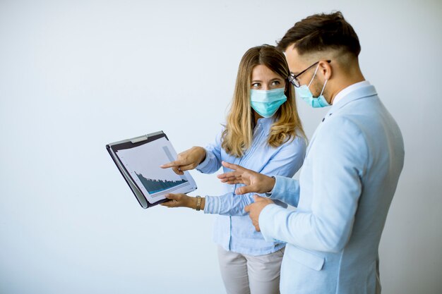 Geschäftspartner, die im Büro stehen und Geschäftsergebnisse betrachten, während sie Gesichtsmasken tragen, sind ein Virenschutz