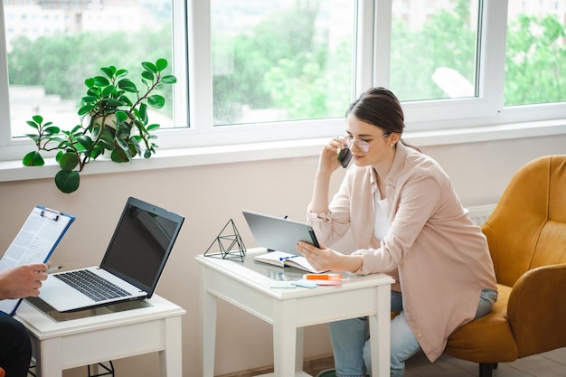 Geschäftspartner, die von zu Hause aus mit Laptop arbeiten, während sie in einem Aramchair sitzen, Frau, die am Telefon spricht ...