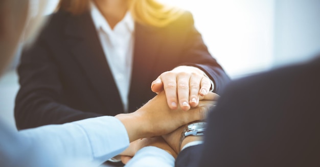 Geschäftsteam, das Einheit mit ihren Händen zusammen im sonnigen Büro zeigt. Gruppe von Menschen, die sich an den Händen halten und das Konzept der Freundschaft, Teamarbeit und Partnerschaft darstellen.