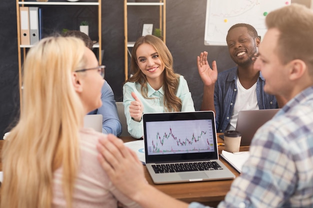 Geschäftsteam, das über Ergebnisse ihrer Arbeit spricht. Gruppe fröhlicher Geschäftsleute, die Diagramme auf dem Laptop studieren, neue Marketingstrategien diskutieren, im Büro sitzen, Platz kopieren