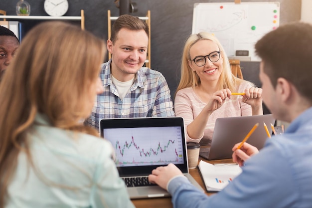 Geschäftsteam, das über Ergebnisse ihrer Arbeit spricht. Gruppe fröhlicher Geschäftsleute, die Diagramme auf dem Laptop studieren, neue Marketingstrategien diskutieren, im Büro sitzen, Platz kopieren