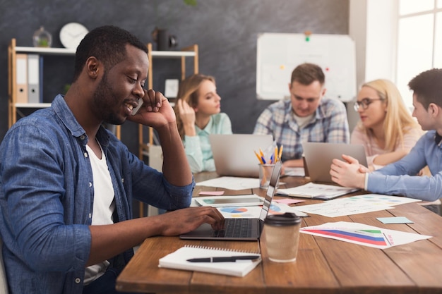 Geschäftsteam, das über Ergebnisse ihrer Arbeit spricht. Gruppe fröhlicher Geschäftsleute, die über neue Marketingstrategie diskutieren, junger schwarzer Mann, der am Telefon spricht, Kopienraum