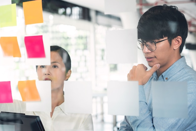 Geschäftsteamarbeit in Besprechung und Haftnotiz auf Spiegelplatte, die mit Team im Büroraum für das Sammeln eines Ideen-Brainstorming-Plans besprochen wird.