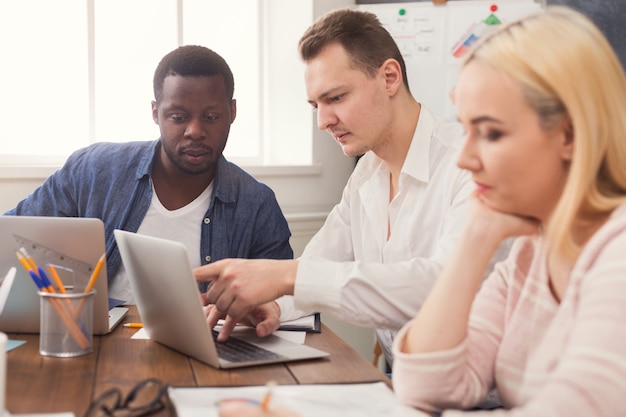 Geschäftstreffen des jungen multiethnischen Teams. Bürodiskussion über neues Projekt, afroamerikanischer Mann, der mit Partner im Büro kommuniziert, Kopierraum