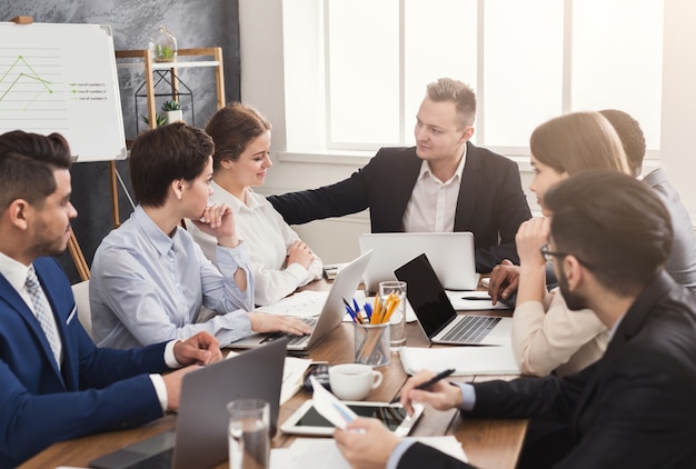 Geschäftstreffen des jungen Teams. Fröhliche Leute, die Brainstorming betreiben, über erfolgreiche Verträge und großen Gewinn im Büro diskutieren, Platz kopieren