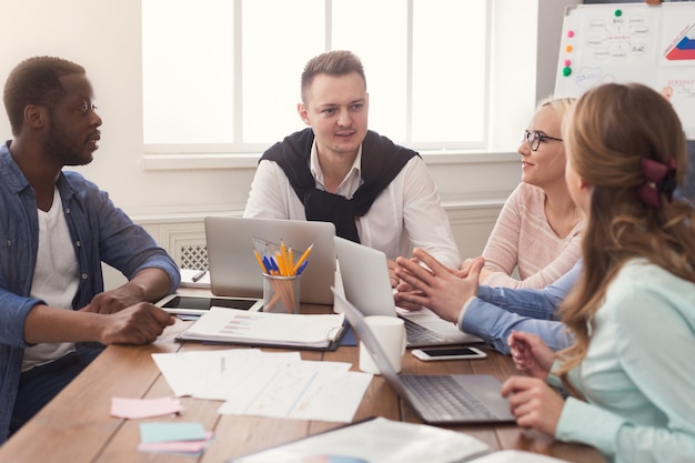 Geschäftstreffen des multiethnischen Teams. Junge, fröhliche Leute, die Brainstorming machen, neues Startup-Projekt im Büro diskutieren, Raum kopieren