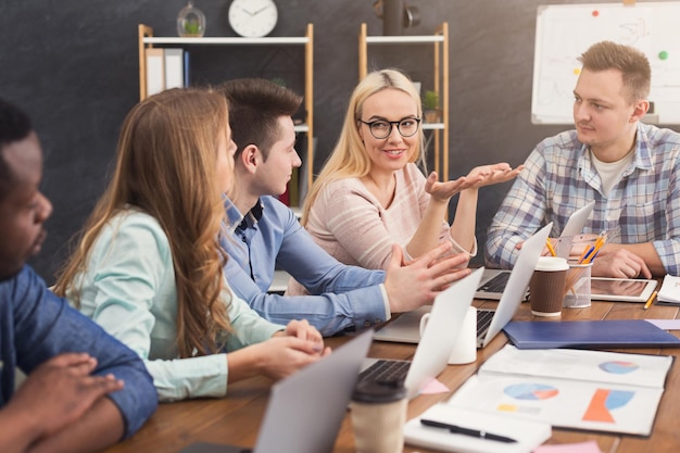 Geschäftstreffen des multiethnischen Teams. Junge, fröhliche Leute, die Brainstorming machen, neues Startup-Projekt im Büro diskutieren, Raum kopieren