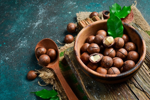 Geschälte Macadamia-Nüsse und geschälte Macadamia-Nüsse auf schwarzem Hintergrund in einem Holzlöffel