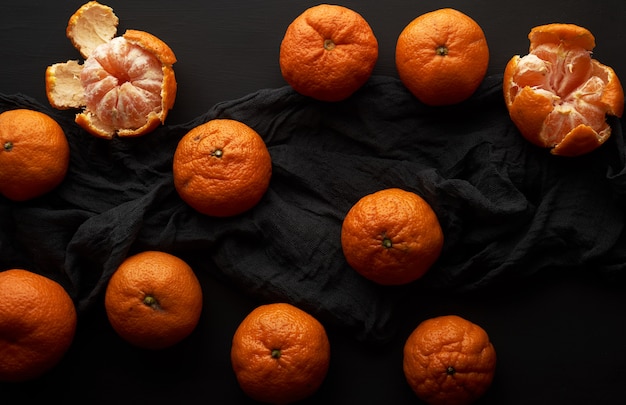 Geschälte reife Orangenmandarine und ein Bündel ungeschälte runde ganze Früchte auf einer schwarzen Serviette