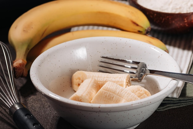 Geschälte und zerbrochene Bananen in Keramikschüssel Zutat zum Kochen von Bananenbrot auf braunem Hintergrund