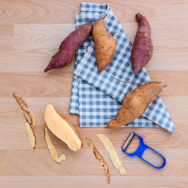 Geschälte zwei Vielzahl der Süßkartoffeln mit Schäler auf rustikaler hölzerner Tabelle.