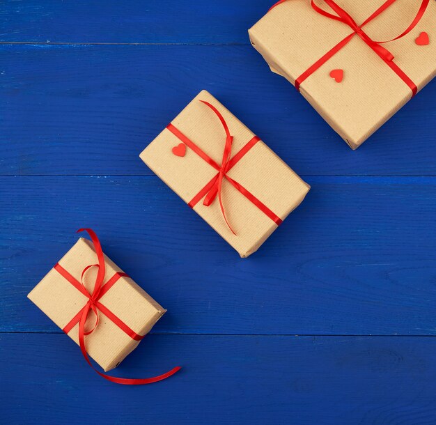 Geschenk eingewickelt im braunen Kraftpapier und mit einem dünnen roten Band auf einem blauen hölzernen Hintergrund gebunden