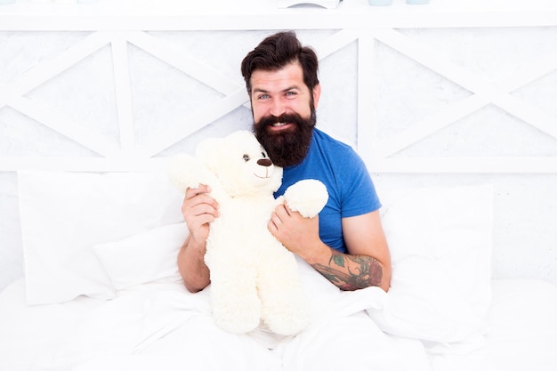 Geschenk für Ehepartner. Süßes Teddybär-Spielzeug. Weichheit Zärtlichkeit. Verspielter Erwachsener. Süß und romantisch. Bärtiges Hipster-Spielzeug. Valentinstagsgeschenk. Mann umarmt weiches Spielzeug, das sich im Bett entspannt. Machen Sie ein Überraschungskonzept.