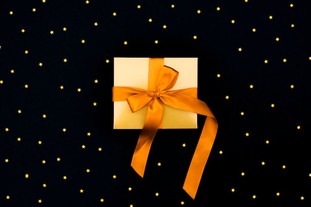 Foto geschenk goldbox mit einer orange satinschleife auf dem schwarzen hintergrund mit vielen kleinen sternen.