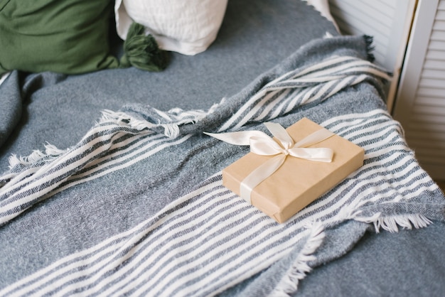 Geschenk in Bastelpapier, gebunden mit einem beigen Satinband, liegt auf der Decke auf dem Bett