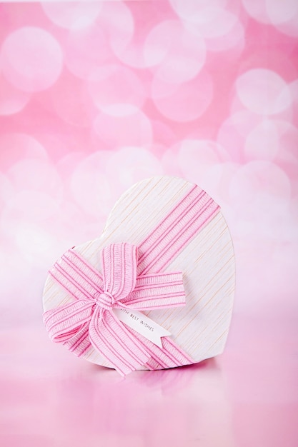 Geschenk mit einem Bogen in Form eines Herzens auf einem rosa Hintergrund mit Bokeh