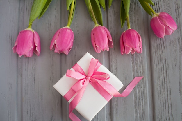 Foto geschenk mit rosa schleife und rosa tulpen auf dem grauen hölzernen hintergrund