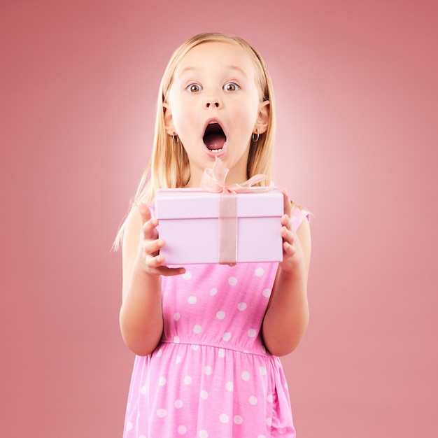 Geschenk und Wow-Porträt eines Kindes im Studio für einen Geburtstag oder eine glückliche Feier Aufgeregtes Mädchen auf einem rosa Hintergrund mit offenem Mund und einem erstaunlichen Überraschungspreis in einer Schachtel