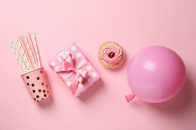 Geschenkbox, Ballon, Cupcake und Pappbecher mit Strohhalmen auf rosa Hintergrund, Draufsicht